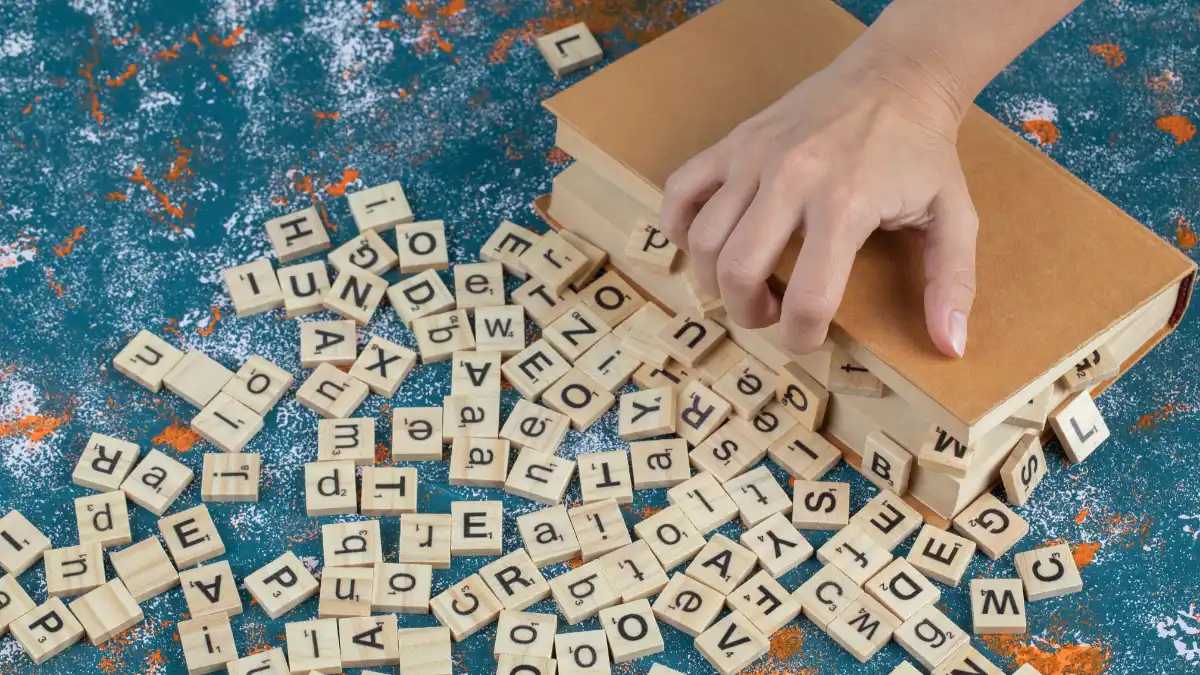 mão pegando letras de madeira espalhadas sobre livros representando palavras no plural da língua portuguesa