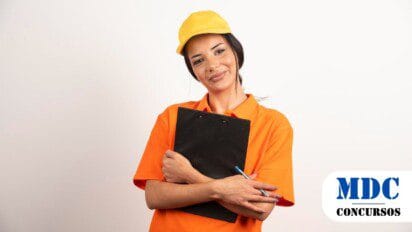 Mulher jovem com pele clara vestindo uniforme laranja e boné amarelo, segurando um prancheta preta e uma caneta azul. Ela sorri levemente e olha para a câmera. O fundo é branco, e a iluminação é suave e equilibrada / Alto Horizonte - GO abre Processo Seletivo com 280 vagas e salários de até R$3,3 mil