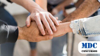 Mãos de várias pessoas empilhadas umas sobre as outras em um gesto de união e trabalho em equipe. Os diferentes tons de pele e estilos de roupas sugerem diversidade. A imagem transmite colaboração e solidariedade / Catalão GO abre 74 vagas em Processo Seletivo com salários de até R$ 7,5 mil