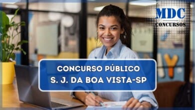 A imagem mostra uma mulher jovem de pele morena e cabelos cacheados, sorrindo enquanto trabalha em um ambiente moderno e bem iluminado. Ela está vestindo uma camisa social azul clara e segura uma caneta sobre um documento com gráficos coloridos. Um laptop aberto está sobre a mesa de madeira ao seu lado. O fundo apresenta um espaço de escritório ou coworking, com paredes de vidro, decoração colorida e algumas plantas. A cena transmite um ambiente profissional e produtivo / Concurso em São João da Boa Vista  - SP oferece salários de até R$ 5.070,69