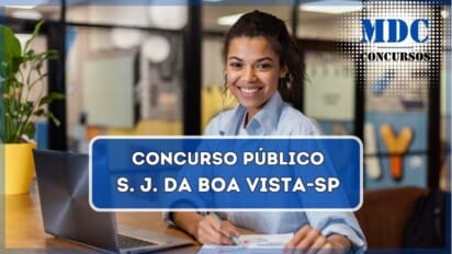 A imagem mostra uma mulher jovem de pele morena e cabelos cacheados, sorrindo enquanto trabalha em um ambiente moderno e bem iluminado. Ela está vestindo uma camisa social azul clara e segura uma caneta sobre um documento com gráficos coloridos. Um laptop aberto está sobre a mesa de madeira ao seu lado. O fundo apresenta um espaço de escritório ou coworking, com paredes de vidro, decoração colorida e algumas plantas. A cena transmite um ambiente profissional e produtivo / Concurso em São João da Boa Vista  - SP oferece salários de até R$ 5.070,69