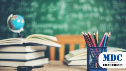 Imagem de um ambiente escolar com um fundo de lousa verde cheia de equações escritas em giz. Em primeiro plano, há um porta-lápis azul com lápis coloridos, livros abertos e fechados sobre uma mesa de madeira. Um pequeno globo terrestre e uma lupa também estão presentes, compondo um cenário de estudo e aprendizado / Oportunidade em Ipueira RN: Processo Seletivo com salários de R$ 5.273,62
