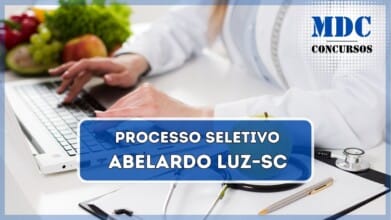 A imagem mostra uma profissional da área da saúde vestindo um jaleco branco enquanto digita em um laptop. Sobre a mesa branca, há um estetoscópio, uma prancheta com folhas de papel, uma caneta dourada e uma maçã verde. Ao fundo, é possível ver uma variedade de frutas e vegetais frescos, incluindo uvas, maçãs e alface, sugerindo uma ênfase em saúde e nutrição / Prefeitura de Abelardo Luz anuncia processo seletivo para cadastro reserva