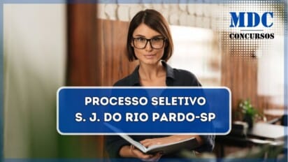 Mulher jovem com cabelos curtos castanhos e óculos de armação preta, vestindo uma camisa escura, segurando um caderno aberto e olhando diretamente para a câmera com uma expressão confiante. O ambiente ao fundo tem uma parede com revestimento de madeira e tijolos brancos, além de móveis e plantas, sugerindo um espaço moderno e aconchegante / Prefeitura de São José do Rio Pardo - SP abre Processo Seletivo com salário de R$ 6.905,41