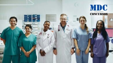 Um grupo de seis profissionais de saúde em um ambiente hospitalar. Eles estão alinhados lado a lado, sorrindo para a câmera. Duas pessoas vestem jalecos brancos com estetoscópios pendurados no pescoço, enquanto as outras quatro usam uniformes médicos coloridos (verde, azul e roxo). Ao fundo, há equipamentos médicos e prateleiras organizadas, sugerindo um ambiente clínico ou hospitalar / Processo Seletivo CIOP Presidente Prudente: 11 vagas e salários de até R$ 4,1 mil; inscrições até domingo (23)