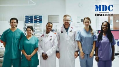 Um grupo de seis profissionais de saúde em um ambiente hospitalar. Eles estão alinhados lado a lado, sorrindo para a câmera. Duas pessoas vestem jalecos brancos com estetoscópios pendurados no pescoço, enquanto as outras quatro usam uniformes médicos coloridos (verde, azul e roxo). Ao fundo, há equipamentos médicos e prateleiras organizadas, sugerindo um ambiente clínico ou hospitalar / Processo Seletivo CIOP Presidente Prudente: 11 vagas e salários de até R$ 4,1 mil; inscrições até domingo (23)