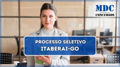 Mulher jovem de cabelos castanhos compridos e pele clara, vestindo um casaco cinza sobre uma blusa branca de gola alta e calça jeans. Ela segura um caderno verde dobrado em uma das mãos e tem uma expressão confiante e amigável. Atrás dela, há um escritório moderno com mesas de madeira, cadeiras pretas, laptops, cadernos e caixas de papelão. O ambiente tem divisórias de vidro com estrutura metálica, permitindo a visão de computadores e mais mesas no fundo. / Processo Seletivo (PSS) em Itaberai - GO oferece 13 vagas e salários atrativos