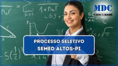 Jovem professora sorridente em pé na frente do quadro-negro segurando o quadro e mostrando o polegar na sala de aula | Processo Seletivo SEMED Prefeitura de Altos (PI): 15 vagas + CR e salários de até R$3 mil