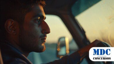 Processos Seletivos 6 Homem dirigindo um veículo ao entardecer, com expressão séria e focada. A luz dourada do pôr do sol ilumina parcialmente seu rosto, enquanto a estrada desfocada é visível através do para-brisa / Processo Seletivo em Balsa Nova PR oferece vaga para motorista