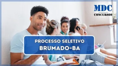 Uma imagem de um grupo de jovens sentados no chão de um corredor iluminado, encostados em uma parede branca. O foco está em um jovem sorridente de camiseta azul clara, segurando uma caneta e um caderno aberto. Atrás dele, quatro jovens estão envolvidos em diferentes atividades, como conversar, usar um laptop e escrever em cadernos. Eles parecem estar estudando ou discutindo algo em um ambiente acadêmico ou universitário. O local tem uma atmosfera descontraída e colaborativa, com fones de ouvido, laptops e materiais de estudo espalhados / Processo Seletivo em Brumado  - BA abre 80 Vagas no Sistema Municipal de Ensino