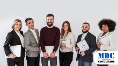 Seis profissionais bem vestidos, de diferentes etnias, posam sorrindo contra um fundo branco. Alguns seguram pastas, laptops ou pranchetas, sugerindo um ambiente corporativo ou de negócios - Barroquinha (CE) Abre 107 Vagas em Processo Seletivo com Salários de Até R$ 8 mil