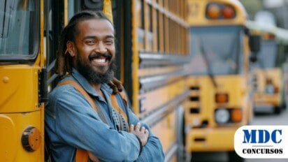 Homem sorridente com cabelos longos e barba encostado em um ônibus escolar amarelo. Ele usa camisa jeans e alças de mochila. Ao fundo, há mais ônibus amarelos estacionados. Imagem gerada por IA / Canhotinho  - PE Abre Processo Seletivo com 110 Vagas na Rede Municipal de Educação