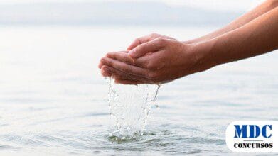 Mãos humanas em concha seguram e deixam escorrer água cristalina de um lago calmo. O fundo desfocado mostra uma paisagem natural. Imagem gerada por IA / Concurso Público ARES-PCJ Abre 10 Vagas com Salários de até R$ 13 mil