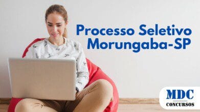 Mulher jovem sentada em uma poltrona vermelha tipo puff, usando um moletom branco com estampa de pássaros e calça bege, segurando um laptop prateado no colo e sorrindo enquanto olha para a tela - Morungaba (SP) Abre Seletivo com 13 Vagas e Salário de R$ 3 Mil