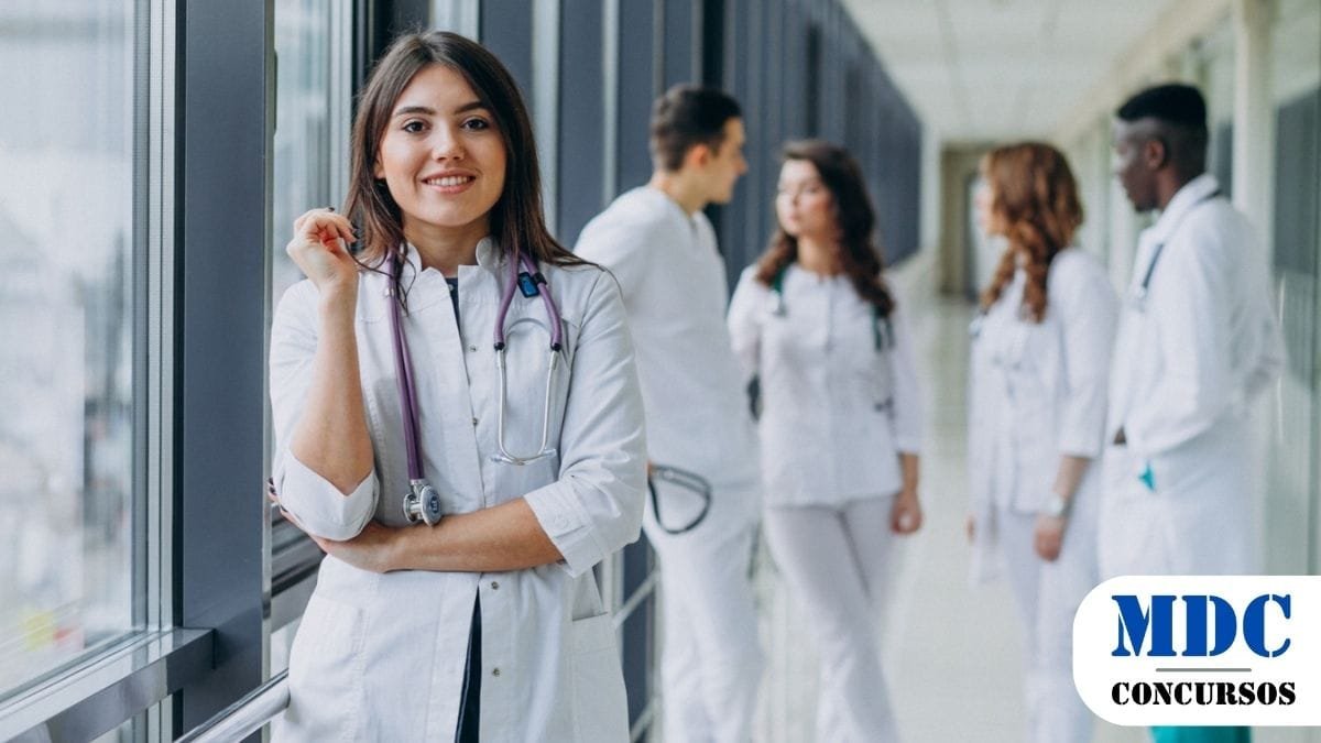 Prefeitura de Careiro da Várzea (AM) lança Processo Seletivo com 229 vagas e salários de até R$ 12,4 mil 1 Grupo de jovens médicos ou estudantes de medicina em um corredor de hospital. No primeiro plano, uma mulher com jaleco branco e estetoscópio roxo sorri para a câmera. Ao fundo, quatro profissionais conversam, todos vestidos de branco, com um deles usando calça verde. O ambiente é iluminado e moderno. Prefeitura de Careiro da Várzea