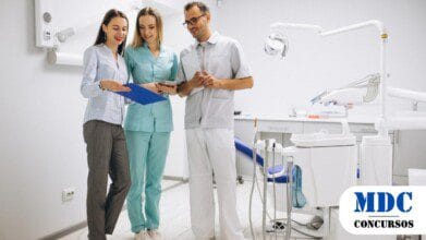 Equipe de profissionais em um consultório odontológico moderno, incluindo um dentista de jaleco branco, uma assistente de uniforme verde e uma mulher de roupa social segurando uma prancheta, todos sorrindo e discutindo informações enquanto analisam documentos e um tablet - Processo Seletivo Capim Grosso (BA) oferece 202 Vagas com Salários de até R$ 4,2 mil