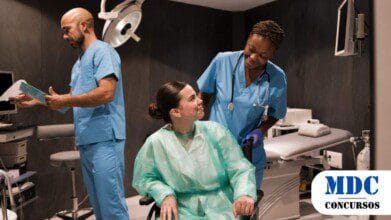 Processos Seletivos 5 Equipe médica em ambiente hospitalar. Enfermeira sorri para paciente em cadeira de rodas, que veste avental descartável. Médico de avental azul segura prontuário e analisa documentos. Sala com equipamentos médicos, maca, monitor e cilindro de oxigênio. Iluminação clínica e atmosfera profissional - Resultado Final do Processo Seletivo 2025 na Saúde de Cruzeiro do Sul é Publicado