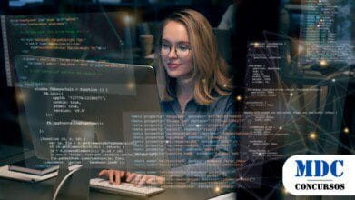 Mulher com óculos e cabelo loiro trabalha em um computador em um ambiente moderno. Códigos e elementos gráficos futuristas aparecem sobrepostos, representando tecnologia e programação - SESI/SENAI Amapá Lançam Processo Seletivo para Analista de TI