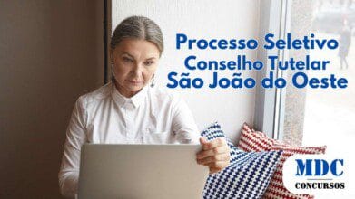 Mulher de cabelo grisalho e blusa branca usa um notebook perto da janela. Texto azul informa sobre o processo seletivo do Conselho Tutelar de São João do Oeste. No canto inferior direito, logotipo do MDC Concursos - São João do Oeste (SC) Abre 3 Vagas para Membro do Conselho Tutelar
