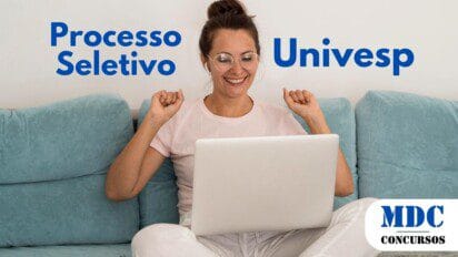Mulher jovem de óculos e fones de ouvido sentada em um sofá azul, vestindo roupas confortáveis e sorrindo animada enquanto usa um laptop branco - Univesp Abre 54 Vagas com Salários de até R$ 7 Mil em novo Processo Seletivo