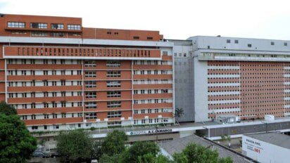 Fachada do Hospital A.C. Camargo, com edifícios de tijolos aparentes e estrutura moderna, rodeado por árvores e com placa de identificação visível.