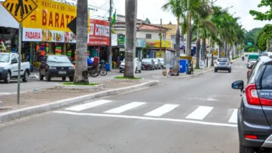 Rua comercial de Abadia de Goiás com faixa de pedestres, carros estacionados, lojas, placas de comércio e palmeiras no canteiro central. Foto: Divulgação/Prefeitura de Abadia de Goiás-GO