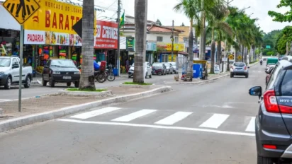 Rua comercial de Abadia de Goiás com faixa de pedestres, carros estacionados, lojas, placas de comércio e palmeiras no canteiro central. Foto: Divulgação/Prefeitura de Abadia de Goiás-GO