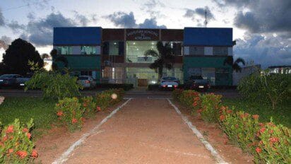 Fachada da Prefeitura Municipal de Acrelândia ao entardecer, com jardins floridos e carros estacionados em frente ao prédio.