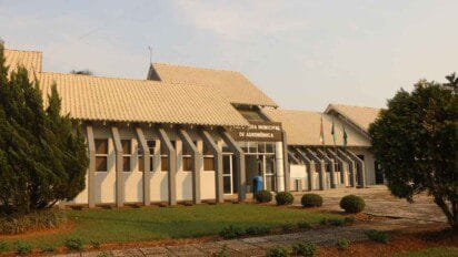 Fachada da Prefeitura Municipal de Agronômica-SC com jardim em primeiro plano e bandeiras ao lado da entrada. Foto: Divulgação/Prefeitura de Agronômica-SC