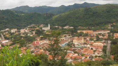 Vista panorâmica da cidade de Águas da Prata SP, com casas, igreja e vegetação cercada por morros verdes.
