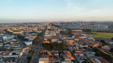 Vista aérea de Alfenas com áreas urbanas, ruas alinhadas, casas e prédios ao fundo, além de campos abertos e montanhas no horizonte ao entardecer. Foto: Divulgação/Prefeitura de Alfenas-MG