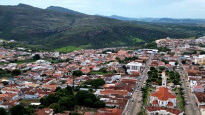 Vista aérea de Alpinópolis-MG com destaque para a igreja matriz, áreas residenciais com telhados vermelhos e montanhas ao fundo.
