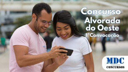 Homem de óculos e camiseta rosa e mulher de blusa branca e cabelos longos e lisos olham sorrindo para um smartphone que ele segura, em um ambiente urbano ao ar livre com pessoas ao fundo - Alvorada do Oeste (RO) convoca 60 aprovados em Concurso de 2024