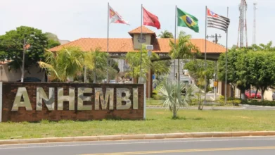 Entrada da cidade de Anhembi/SP com portal ao fundo, bandeiras hasteadas, paisagismo com palmeiras e placa em destaque com o nome ANHEMBI. Foto: Divulgação/https://leianoticias.com.br/