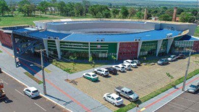 Processos Seletivos 3 Vista aérea do Paço Municipal Senador Ramez Tebet em Bataguassu-MS, com fachada moderna, estacionamento e área verde ao redor.