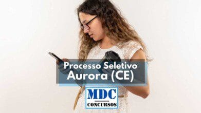 Processos Seletivos 7 Mulher jovem de cabelos ondulados e longos segura um celular em uma mão e um copo térmico na outra, enquanto observa a tela com atenção. Ao centro da imagem, há uma faixa com os dizeres "Processo Seletivo Aurora (CE)" e abaixo o logotipo "MDC Concursos". A imagem é usada para divulgar seleção pública com 120 vagas em Aurora, Ceará.