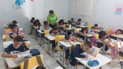Sala de aula com professora acompanhando alunos do ensino fundamental sentados em carteiras, realizando atividades escritas em cadernos e livros escolares. Foto: Divulgação/Instituto Alfa e Beto