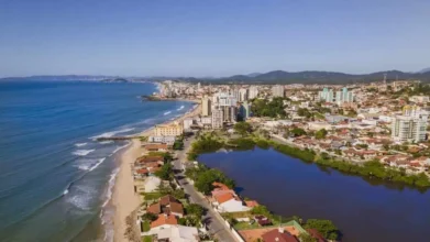 Processos Seletivos 2 Vista aérea de cidade litorânea com praia, prédios, casas e lagoa próxima à orla. Foto: Divulgação/Prefeitura de Barra Velha-SC