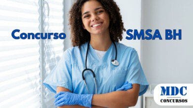 Enfermeira jovem de pele morena e cabelos cacheados sorri enquanto cruza os braços, vestindo uniforme azul, luvas descartáveis e estetoscópio no pescoço. Ela está em um ambiente clínico bem iluminado, próximo a uma janela com persianas brancas - Belo Horizonte abre 582 Vagas e Remuneração de até R$ 11,7 mil na Saúde