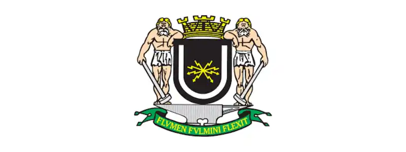 Câmara de Volta Redonda/RJ abre concurso com 11 vagas imediatas 1 Brasão oficial da cidade de Volta Redonda - RJ com dois homens segurando escudos, coroa mural dourada no topo e faixa com o lema "FLVMEN FVLMINI FLEXIT" na base.