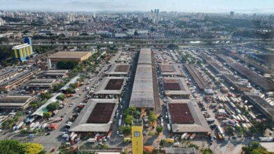 Processos Seletivos 8 Vista aérea do entreposto da CEAGESP em São Paulo, com galpões, caminhões e prédios ao fundo.