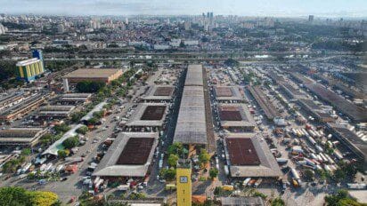 Vista aérea do entreposto da CEAGESP em São Paulo, com galpões, caminhões e prédios ao fundo.