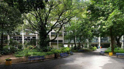 Vista do pátio arborizado do CEFET/RJ, com bancos azuis, jardins e prédio da instituição ao fundo.
