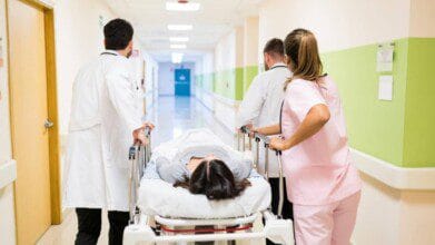 Equipe médica empurrando uma maca com paciente deitada em corredor de hospital.