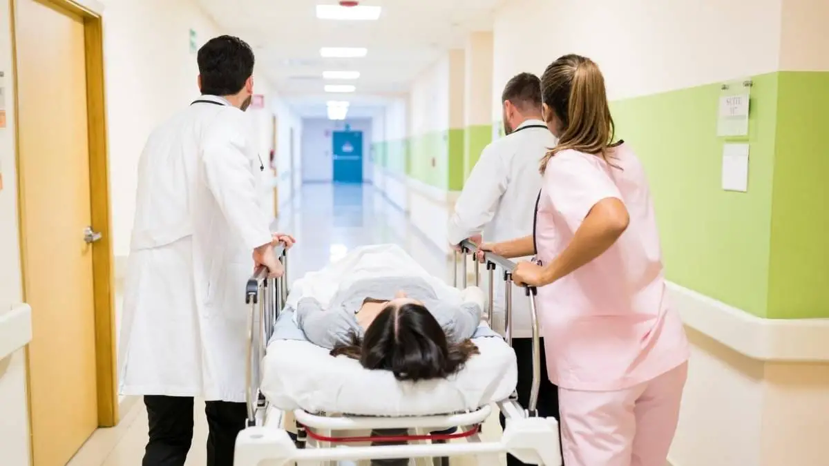 Equipe médica empurrando uma maca com paciente deitada em corredor de hospital.