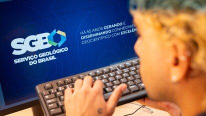 Pessoa utilizando teclado em frente a monitor com logotipo do Serviço Geológico do Brasil e texto institucional comemorando 55 anos.