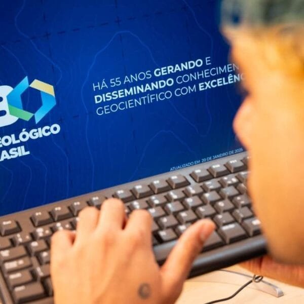 Pessoa utilizando teclado em frente a monitor com logotipo do Serviço Geológico do Brasil e texto institucional comemorando 55 anos.
