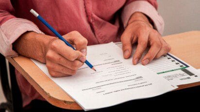 Pessoa preenchendo prova em carteira escolar com lápis azul. Foto: azerbaijan_stockers/Freepik