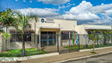 Fachada da Câmara Municipal de Arceburgo-MG com portão gradeado, bandeiras hasteadas e céu azul com nuvens ao fundo. Foto: Divulgação/Prefeitura de Arceburgo-MG