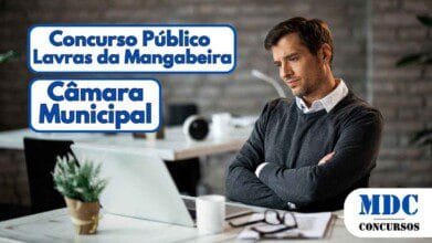 Homem de aparência séria, vestindo suéter cinza sobre camisa branca, está sentado em um escritório moderno com fundo de tijolos aparentes, braços cruzados, olhando para um laptop aberto sobre a mesa. Ao lado, há uma xícara branca, óculos e documentos. O ambiente tem iluminação suave e decoração minimalista com plantas e objetos organizados - Câmara de Lavras da Mangabeira (CE) lança Concurso Público
